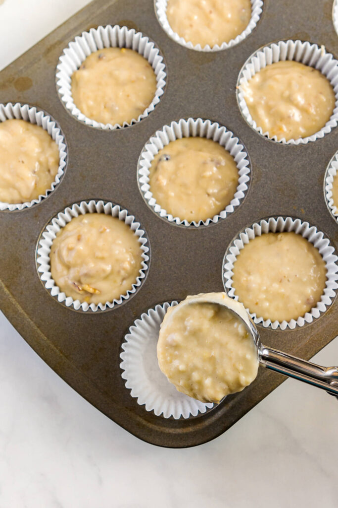 Scooping banana muffin mixture into lined muffin tins using an ice cream scoop